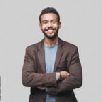 Portrait of handsome smiling young man with folded arms. Laughing joyful cheerful men with crossed hands studio shot. Isolated on gray background